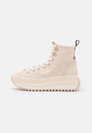 Baskets montantes beiges avec une semelle plateforme épaisse, des lacets blancs, des œillets métalliques, une languette noire au talon et une semelle extérieure dentelée pour une meilleure adhérence.