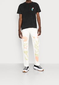 Svart texturerad t-shirt med liten grafik, i kombination med vita byxor med färgglada frukt- och blommönster. Bärs med svarta sneakers.