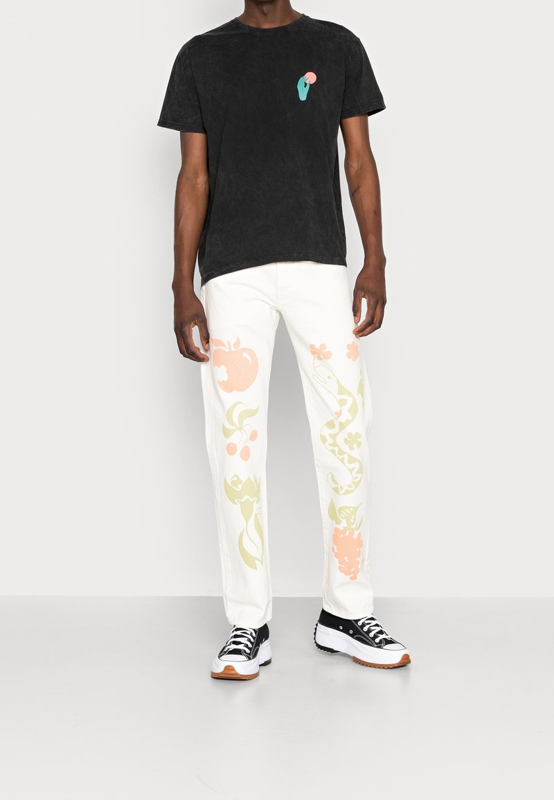 Svart texturerad t-shirt med liten grafik, i kombination med vita byxor med färgglada frukt- och blommönster. Bärs med svarta sneakers.