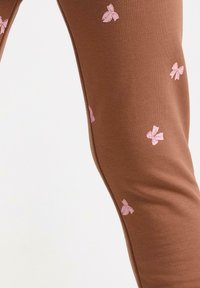 Brune leggings lavet af blødt stof, med lyserøde sløjfeformede mønstre over hele overfladen. Glat tekstur med en tætsiddende pasform.