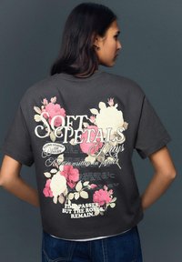 Sötétszürke rövidített póló rózsaszín és krémszínű virágmintákkal, stilizált szöveggel. Rövid ujjú, laza szabású.