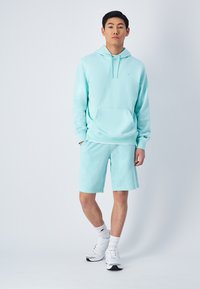 Sudadera de color azul claro con un bolsillo frontal, combinada con pantalones cortos a juego. Confeccionada en tejido suave, cuenta con capucha con cordón y puños acanalados.