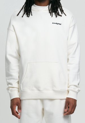 Hooded sweatshirt in white, featuring a front pocket and embroidered black logo. Soft, textured fabric with ribbed cuffs and hem.