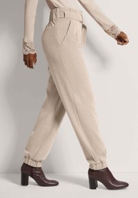 Beige hochtaillierte Hose mit einem Gürtel-Design, schmal zulaufenden Manschetten und seitlichen Taschen, kombiniert mit dunkelbraunen, Absatz-Stiefeletten.