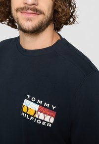 Navy blue langermet genser med et grafisk logo i livlige farger. Myk tekstur med ribbet halslinning og sømmer på skuldrene.