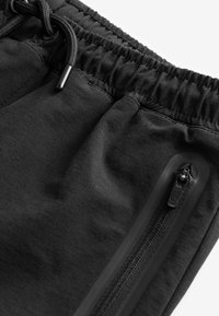 Zwarte sportshorts met een elastische tailleband, een trekkoord en een zijzak met rits, met een gladde textuur.