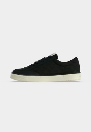 Schwarzer Sneaker in niedriger Ausführung mit schwarzen Schnürsenkeln und dicker, elfenbeinfarbener Gummisohle, von der Seite auf hellem, einfarbigem Hintergrund abgebildet.