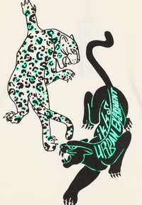 Graafiline T-särk, millel on hüppav leopard rohelistes laigudes ja must panter, musta äärisega, heledal taustal koos tekstiga.