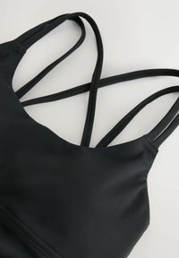 Svart sport-bh med mjukt, stretchy tyg och flera korsade band. Enkelt design utan synliga mönster eller hårdvara.