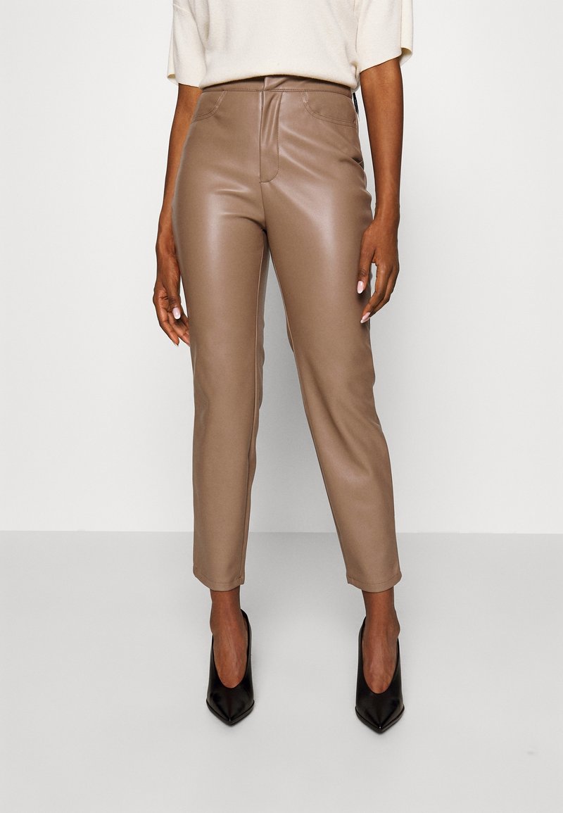 Pantalons en simili cuir marron à taille haute, jambe effilée, poches avant et détails de couture discrets, associés à des escarpins noirs à bout pointu.