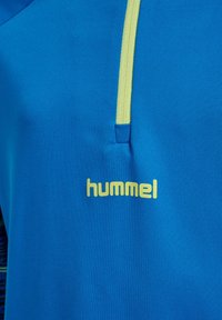 B blaues Sporthemd mit gelben Akzenten und Logo. Hergestellt aus glattem, atmungsaktiven Material mit einem leichten Glanz, entworfen für sportliche Aktivitäten.