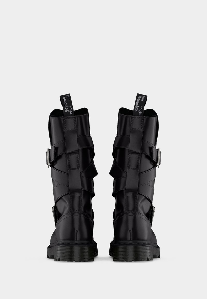 Coppia di stivali da combattimento in pelle nera fino a metà polpaccio con cinturini con fibbia e linguette per tirare con la scritta "WITH SOLES Bouncing" su uno sfondo neutro.