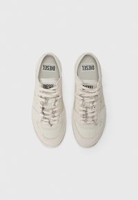 Beige sneakers with a textured fabric and smooth accents. Features metallic hardware on laces, logo on tongue, and rounded toe shape.