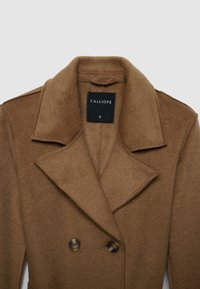 Cappotto in misto lana marrone con design doppiopetto, ampio colletto a risvolto e due bottoni scuri. Etichetta visibile all'interno con il nome del marchio "CALLIOPE."