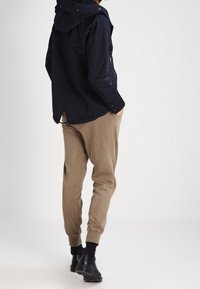 Laivastonsininen hupparitakki, jossa on vetoketjullinen tasku, yhdistettynä vaaleanruskeisiin kapeneviin housuihin. Mustat kengät, joissa on tyylikäs muotoilu, viimeistelevät asun.