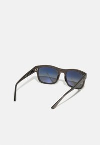 Ochelari de soare din plastic negru cu rame dreptunghiulare, lentile cu gradient albastru și un branding distinctiv pe tâmple. Textură netedă și design modern.