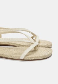 Beiga rep-sandaletter med vävda, korsade remmar, texturerad sål i naturlig fiber, platt fotbädd och en slät brun yttersula.