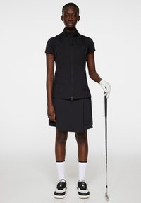 Svart kortärmad golftröja med dragkedja och hög krage, matchad med en svart golfkjol som når knäna. Vita strumpor och svarta golfskor.