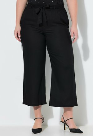 Plus-size person iført sorte, cropped vidde-bukser med bindebånd i taljen og sorte sandaler med hæl og spids snude.