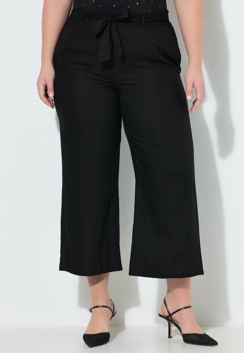 Plus-size person iført sorte, cropped vidde-bukser med bindebånd i taljen og sorte sandaler med hæl og spids snude.