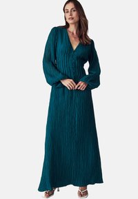 Tannend grüne Maxikleid aus strukturiertem Stoff, mit langen, luftigen Ärmeln, einem V-Ausschnitt und Knöpfen an der Vorderseite. Der Rock fällt frei bis zu den Knöcheln.