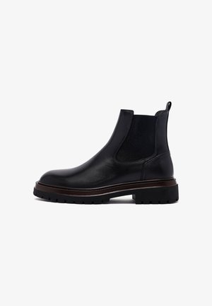 Bottines Chelsea en cuir noir avec des panneaux élastiques sur les côtés, un talon renforcé et une semelle texturée et robuste avec une légère touche de brun.