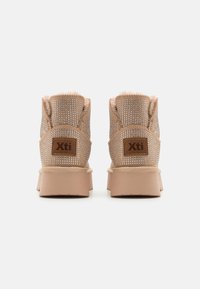 Botas de tobillo beige con parte superior de malla, acentos decorativos de tachuelas, borde de piel sintética y suela de goma marrón claro. Etiqueta de la marca en la parte posterior.