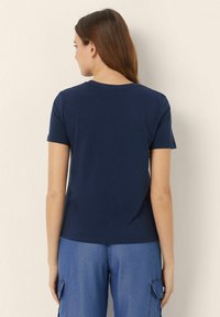 Tricou din bumbac de culoare albastru marin, cu mâneci scurte, decolteu rotund și o croială lejeră. Textură netedă, fără modele sau accente vizibile.