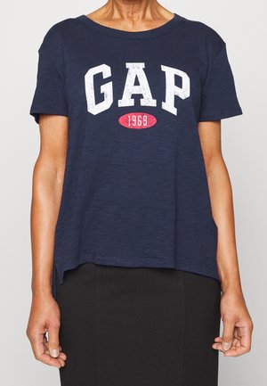 Granatowy bawełniany T-shirt z krótkimi rękawami, z białym logo "GAP" i czerwonym rokiem "1969". Okrągły dekolt i boczne rozcięcia.