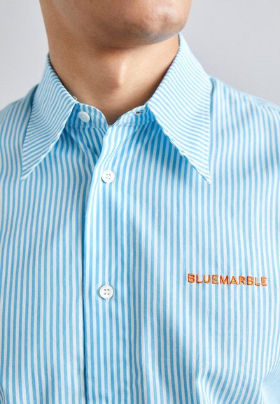 Camisa de botones a rayas azul claro, con cuello amplio, que presenta botones blancos y bordado en naranja "BLUEMARBLE" en el lado izquierdo.