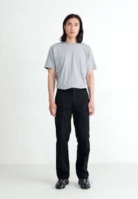 Un tricou gri cu mânecă scurtă, pantaloni negri drepți și adidași negri. Design simplu, minimalist, fără modele sau accente vizibile.