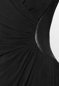 Černé šaty s plisovaným materiálem a hladkými koženými akcenty. Design předvádí přiléhavou siluetu a kontrastní textury.