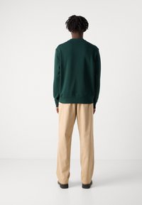 Felpa verde con colletto e polsini a coste, abbinata a pantaloni beige a vita alta e larghi. Design minimalista, vista da dietro.