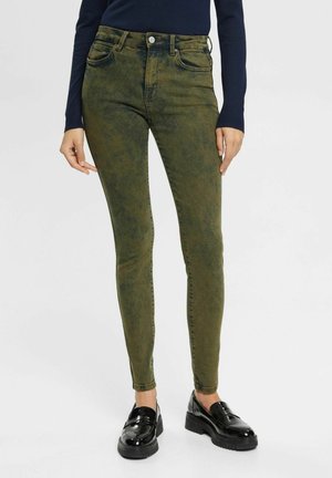 Jeans skinny vert olive avec une texture délavée, design à cinq poches et fermeture à boutons. Associés à des mocassins noirs brillants.