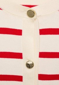 Krémový kardigan s červenými horizontálními pruhy, s kulatým výstřihem a zlatým zapínáním na knoflík vpředu. Měkká pletená textura.