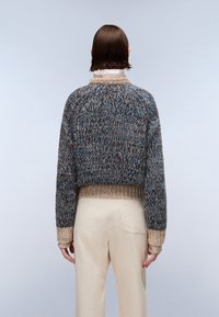 Skórzany sweter z wielokolorowym wzorem w odcieniach niebieskiego, brązowego i beżowego, z prążkowanym dołem i kontrastowymi ściągaczami.