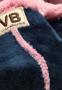 Material de forro polar en color azul marino con una costura de acento rosa. Presenta un parche de logo marrón que dice "VB vulcabicha". Textura suave y diseño esponjoso.