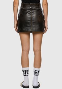 Mini-jupe en cuir noir, ajustée avec une texture lisse, comportant une couture frontale et deux poches arrière, associée à des chaussettes blanches avec logo.