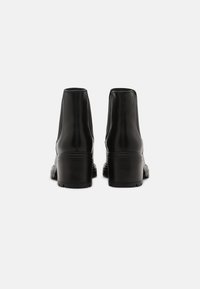 Svarta ankelskor med en slät läderfinish, en lätt utsvängd klack och dubbla sömmar på baksidan, som visar en elegant design.