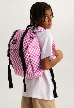 Young person with braided hair wearing a white t-shirt and beige shorts carries pink and white checkered backpack with black straps.