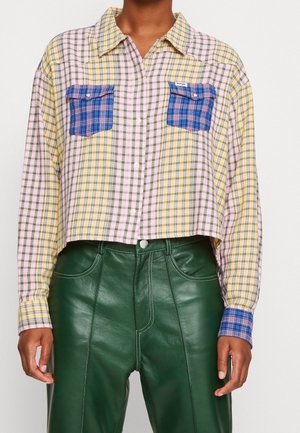 Camicia a quadri corta con check gialli, rosa e verdi; presenta due tasche a quadri blu e chiusura con bottoni. Abbinata a pantaloni in pelle verdi.
