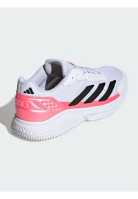 Chaussure de course Adidas blanche avec des rayures noires et un accent rose au talon, présentée en angle pour montrer les détails latéraux et arrière sur un fond clair.