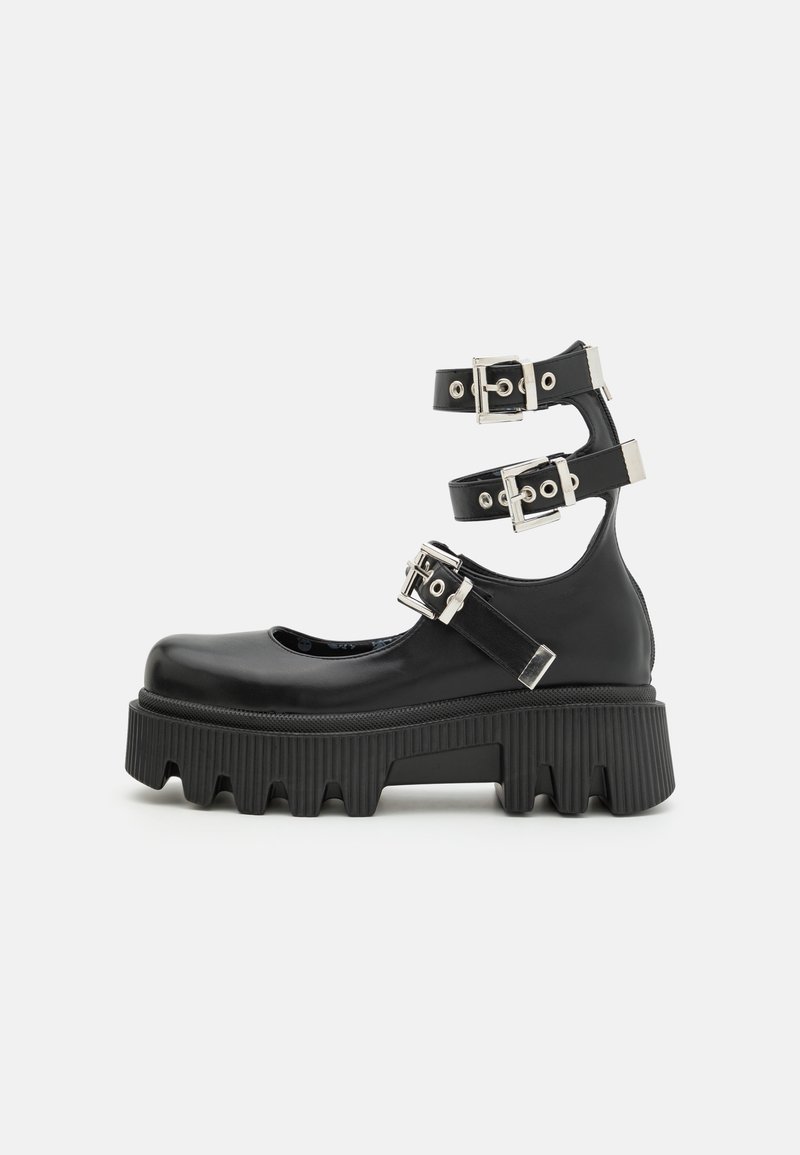 Chaussure plateforme noire avec semelle épaisse rainurée et trois brides réglables à la cheville avec boucles argentées et détails métalliques.