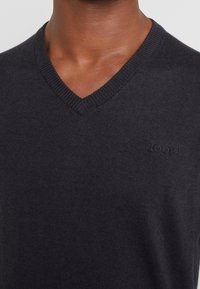 Maglione grigio scuro a collo a V realizzato in tessuto liscio con rifinitura a coste sul colletto; presenta un logo in rilievo discreto sul petto.