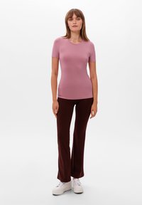 Růžové krátké rukávové přiléhavé tričko v kombinaci s hnědými rozšířenými kalhotami; model má na sobě bílé platformové tenisky; hladká textura látky.