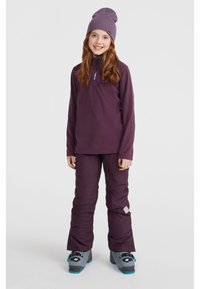 Lila långärmad tröja med halvdragkedja och logga, parat med matchande lila skidbyxor. Avslutat med en lila mössa och grå skidstövlar.