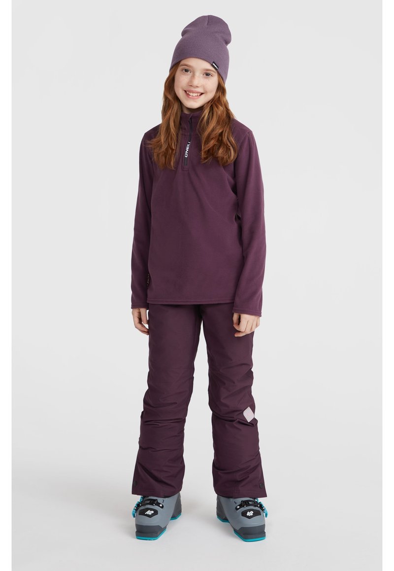 Lila långärmad tröja med halvdragkedja och logga, parat med matchande lila skidbyxor. Avslutat med en lila mössa och grå skidstövlar.