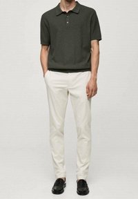 Ciemnozielona koszulka polo z krótkim rękawem w połączeniu z kremowymi spodniami slim fit i czarnymi loafersami. Gładka tkanina z klasycznym kołnierzykiem.