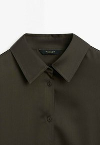 Chemise vert olive foncé avec un col classique et deux boutons visibles à l'avant, montrant une texture de tissu lisse.