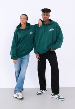 Green hooded sweatshirts with a front pocket and white logo, paired with light blue and black jeans and athletic sneakers.